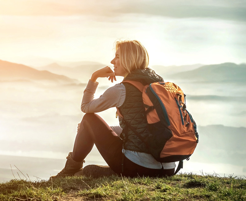 Woman in hiking attire sitting on a mountain top enjoying the view